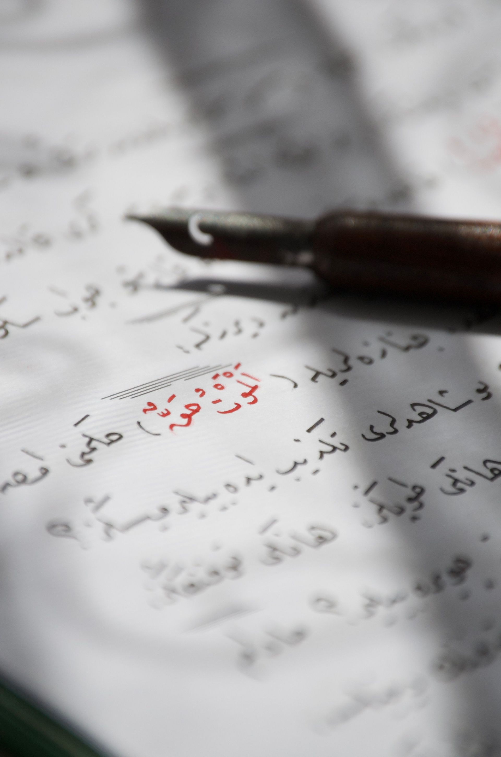 Close-up of a fountain pen on a page with Arabic calligraphy in soft light.